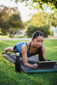 Asian fitness young woman doing planks in the park while she is watching a tutorial on a tablet